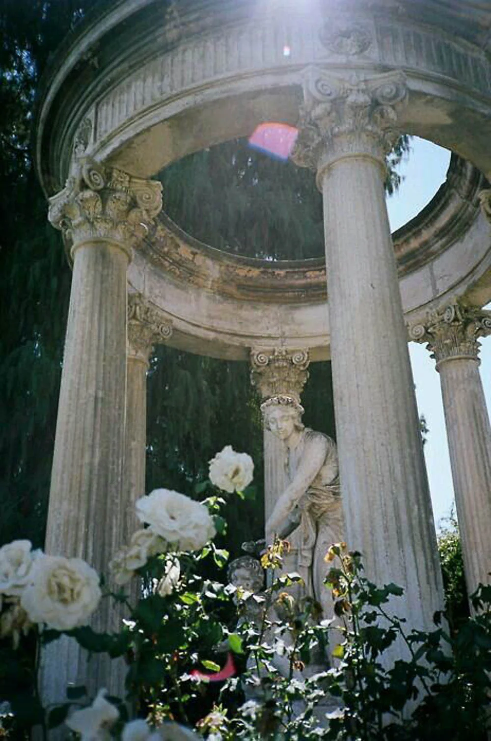 Matte gouache poster painting of a circular stone colonnade monument with a central statue, framed by white roses and sunlit garden foliage in soft sage, ivory and warm stone tones.